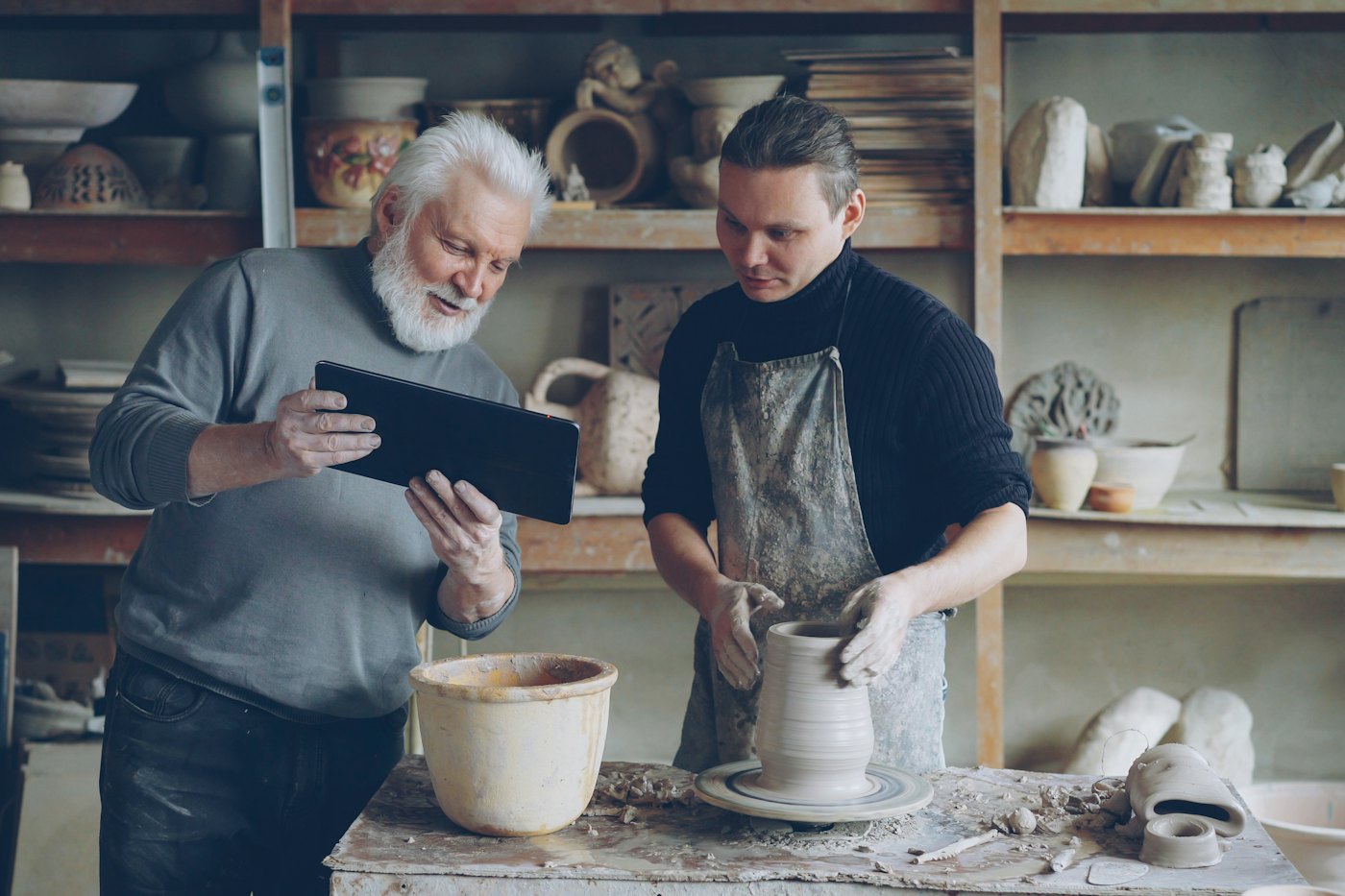 An experienced potter guiding a younger student